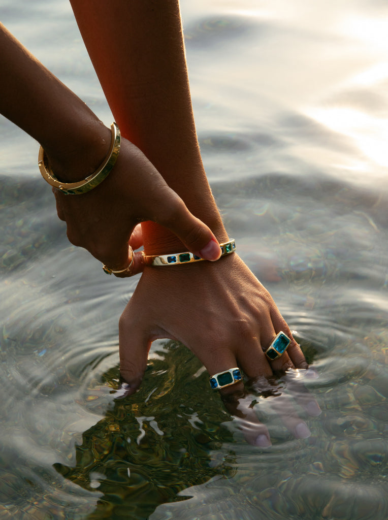 Pulsera de plata dorada rígida abierta con piedras verdes y azules tipo baguette