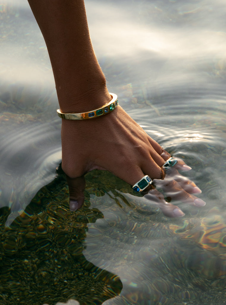 Pulsera de plata dorada rígida abierta con piedras verdes y azules tipo baguette